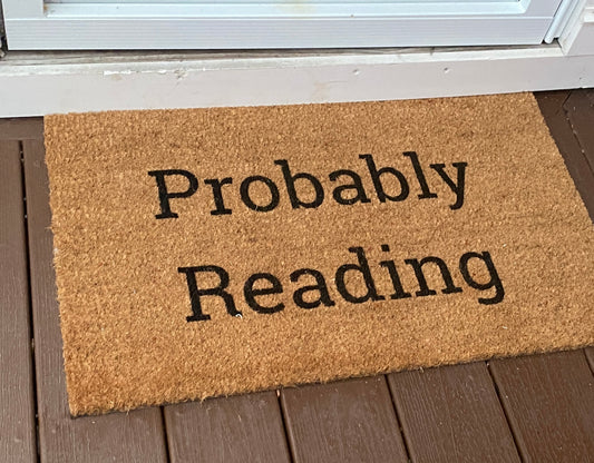 Doormat with 'Probably Reading' text on a wooden floor.